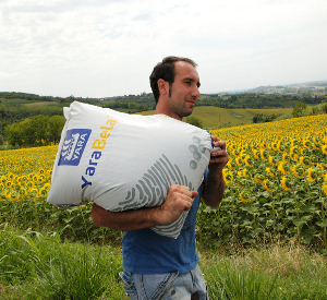 Man carrying a bag of fertiliser keeping head up and back straight to avoid injury